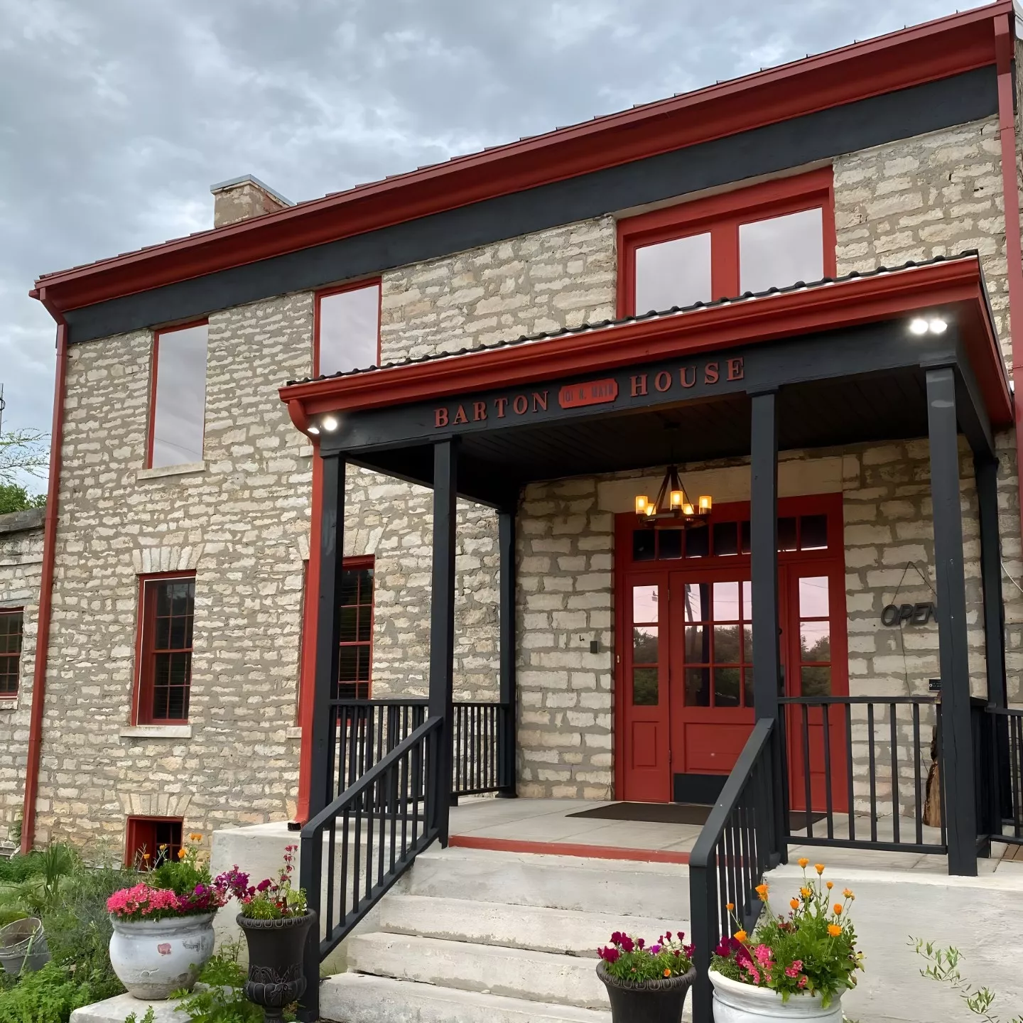 The front entrance to The Barton House of Salado. The historic limestone Barton House features bright red-trimmed windows and a gabled front porch.