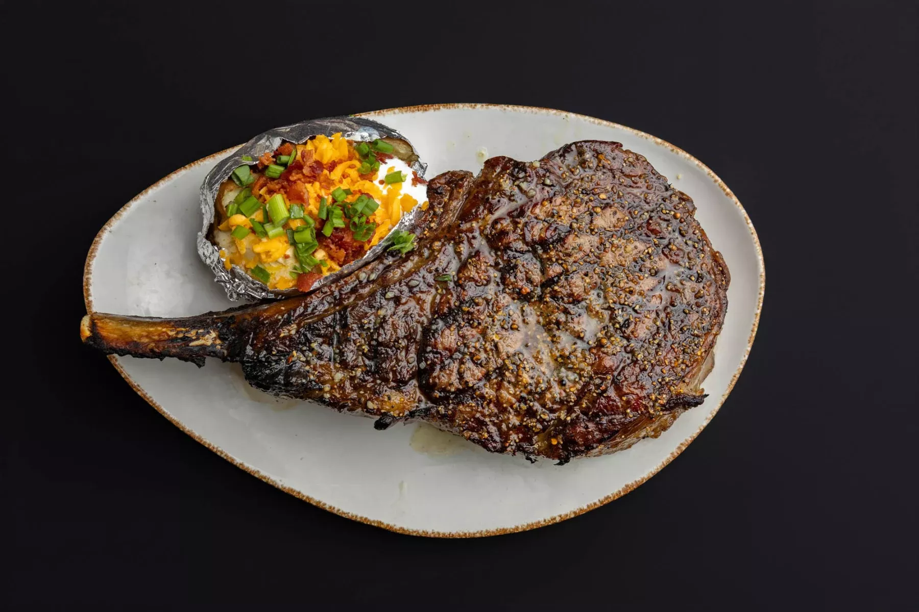 A white plate with a ribeye steak and a side loaded baked potato.